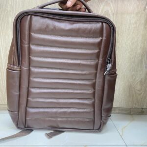 A distinctive brown genuine cow leather backpack featuring a channel-quilted front panel, mesh-backed padded straps, and side pockets. A textured, ergonomic design built for all-day comfort and daily carry.