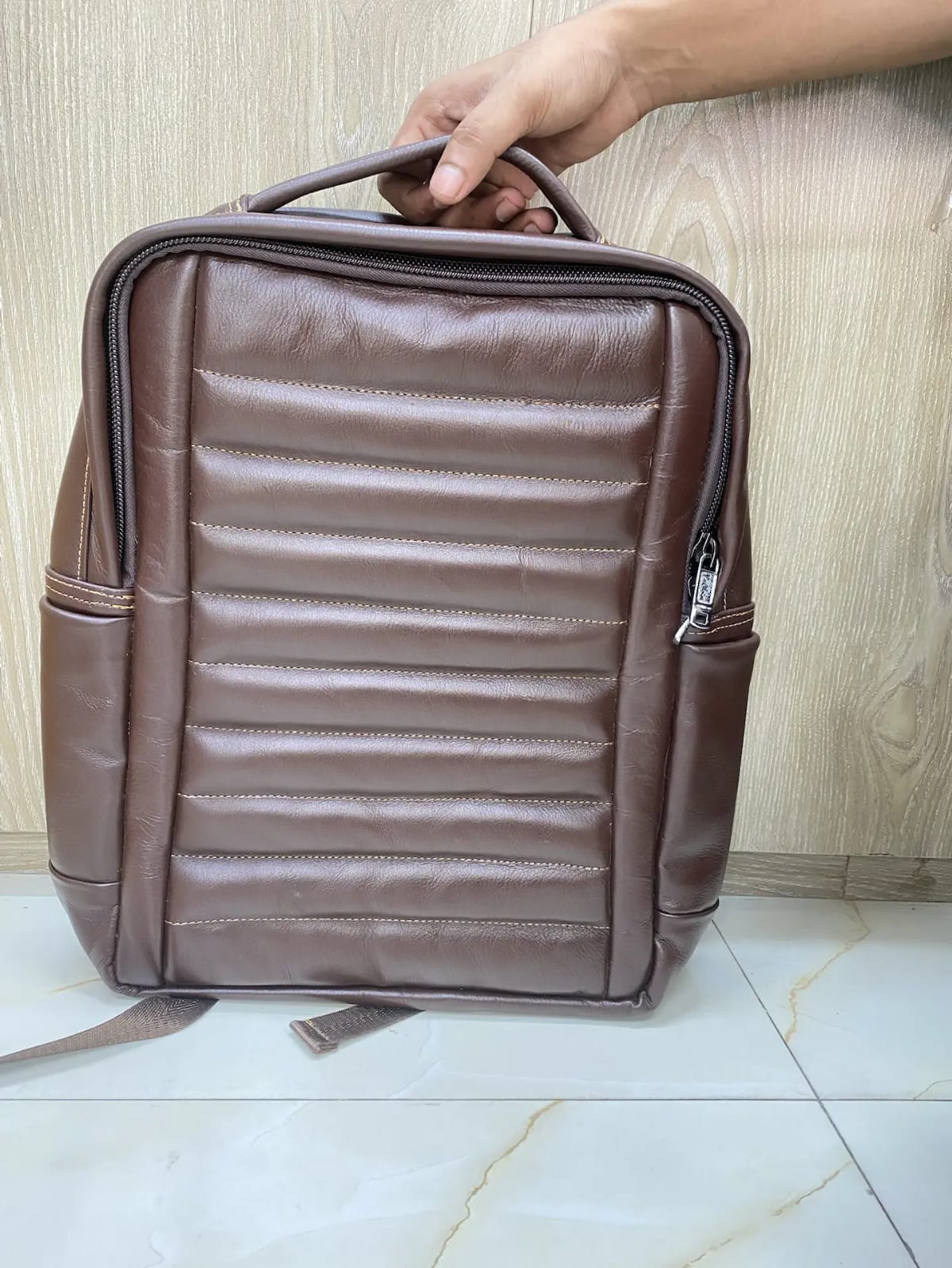 A distinctive brown genuine cow leather backpack featuring a channel-quilted front panel, mesh-backed padded straps, and side pockets. A textured, ergonomic design built for all-day comfort and daily carry.